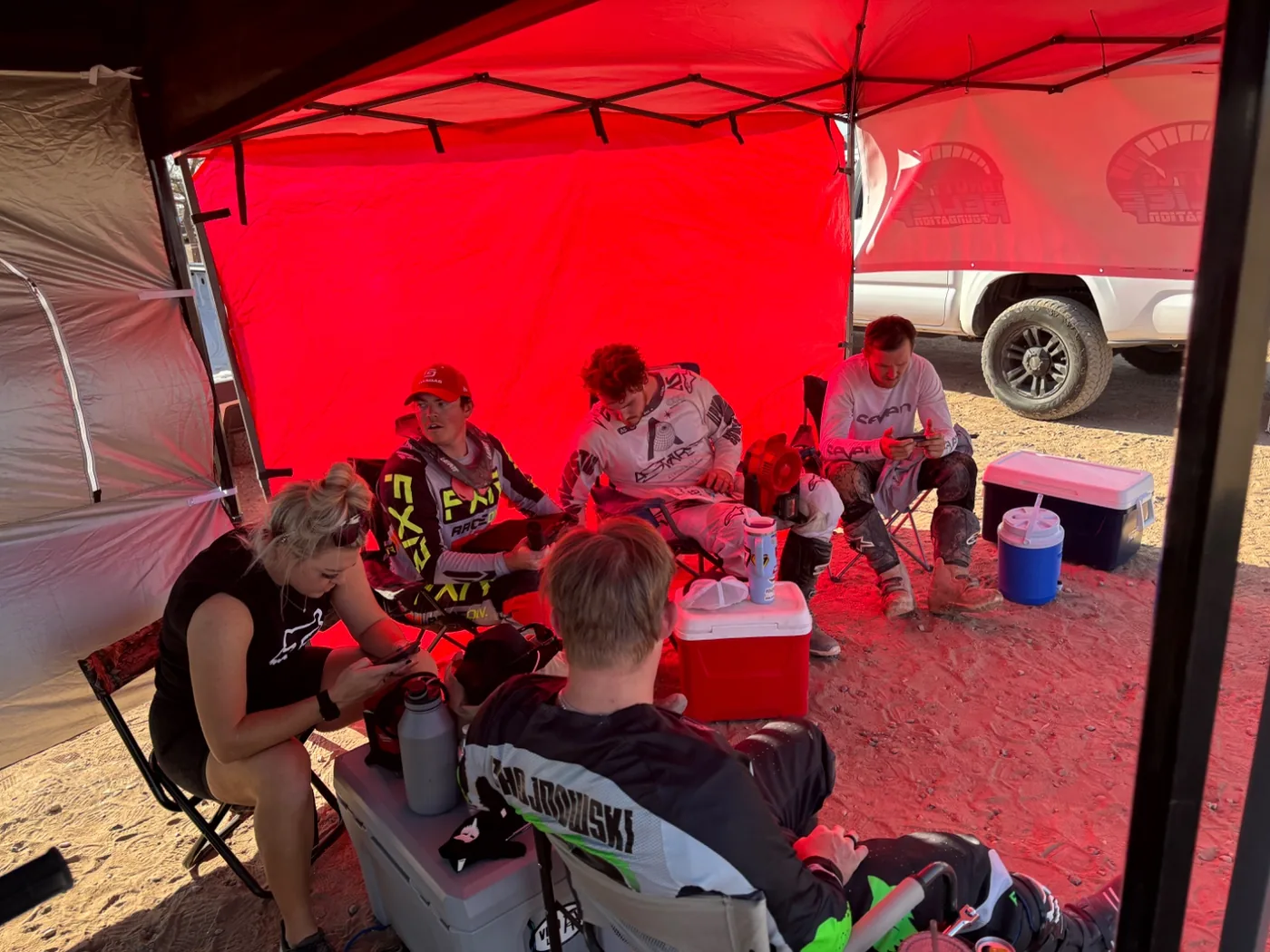 Riders and crew resting together in the pits under a canopy
